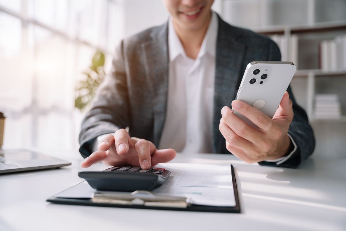 スマートフォンを持ちながら電卓で計算するビジネスマン