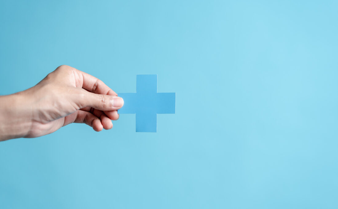青い背景に手が青い十字マークを持っている様子。