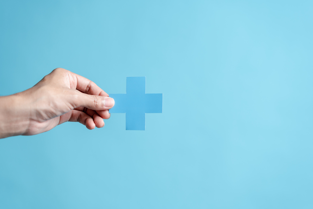 青い背景に手が青い十字マークを持っている様子。