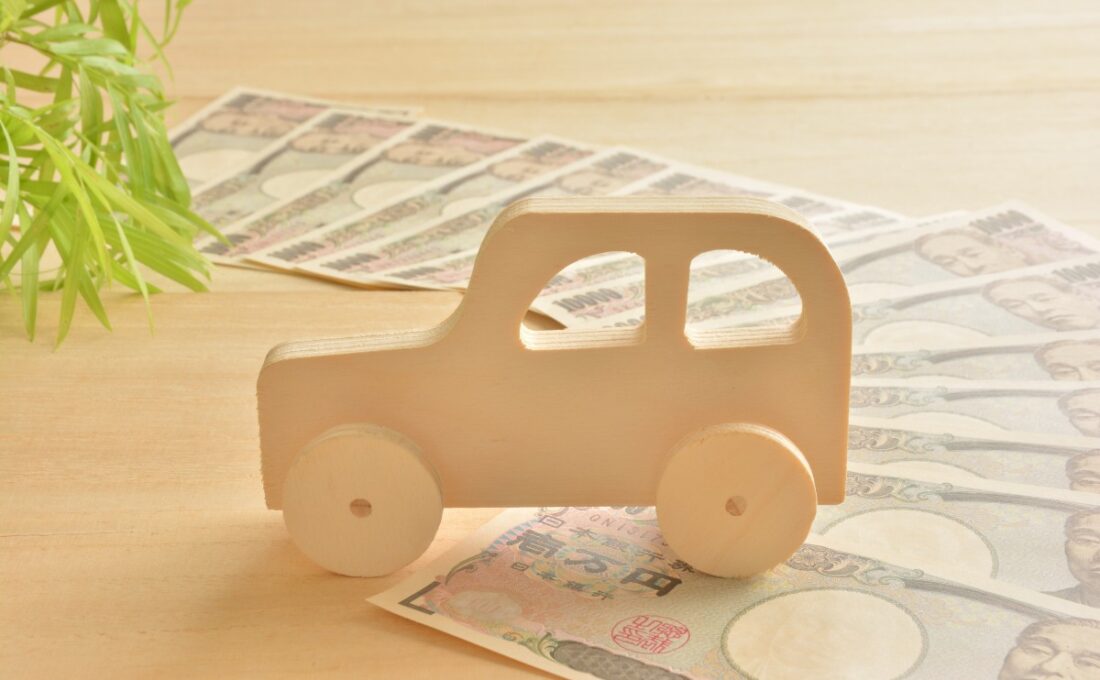 木製の車の模型が、広げられた日本円の紙幣の上に置かれている。