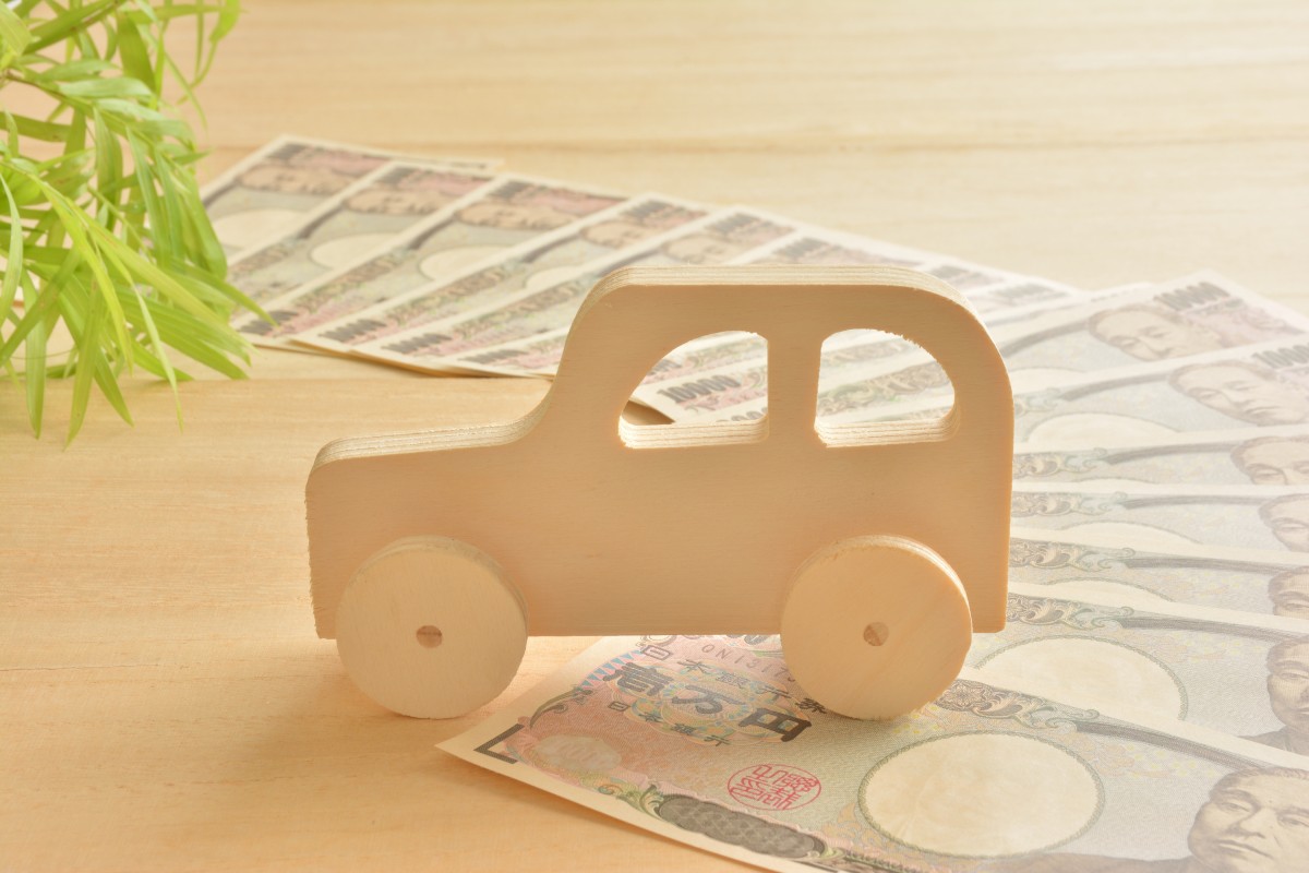 木製の車の模型が、広げられた日本円の紙幣の上に置かれている。