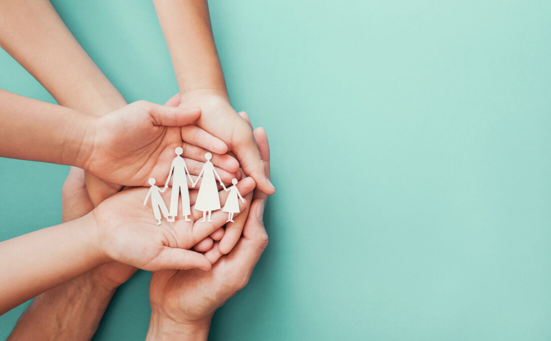 複数の手が、紙で作られた家族の形を持ち上げている様子。