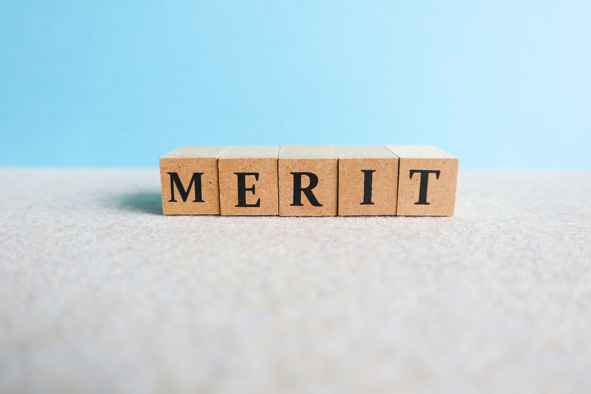 青い背景の前に「MERIT」という文字が書かれた木製ブロックが並べられている。