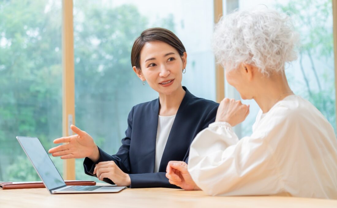 若い女性が年配の女性に対してパソコンを使って説明をしている様子。