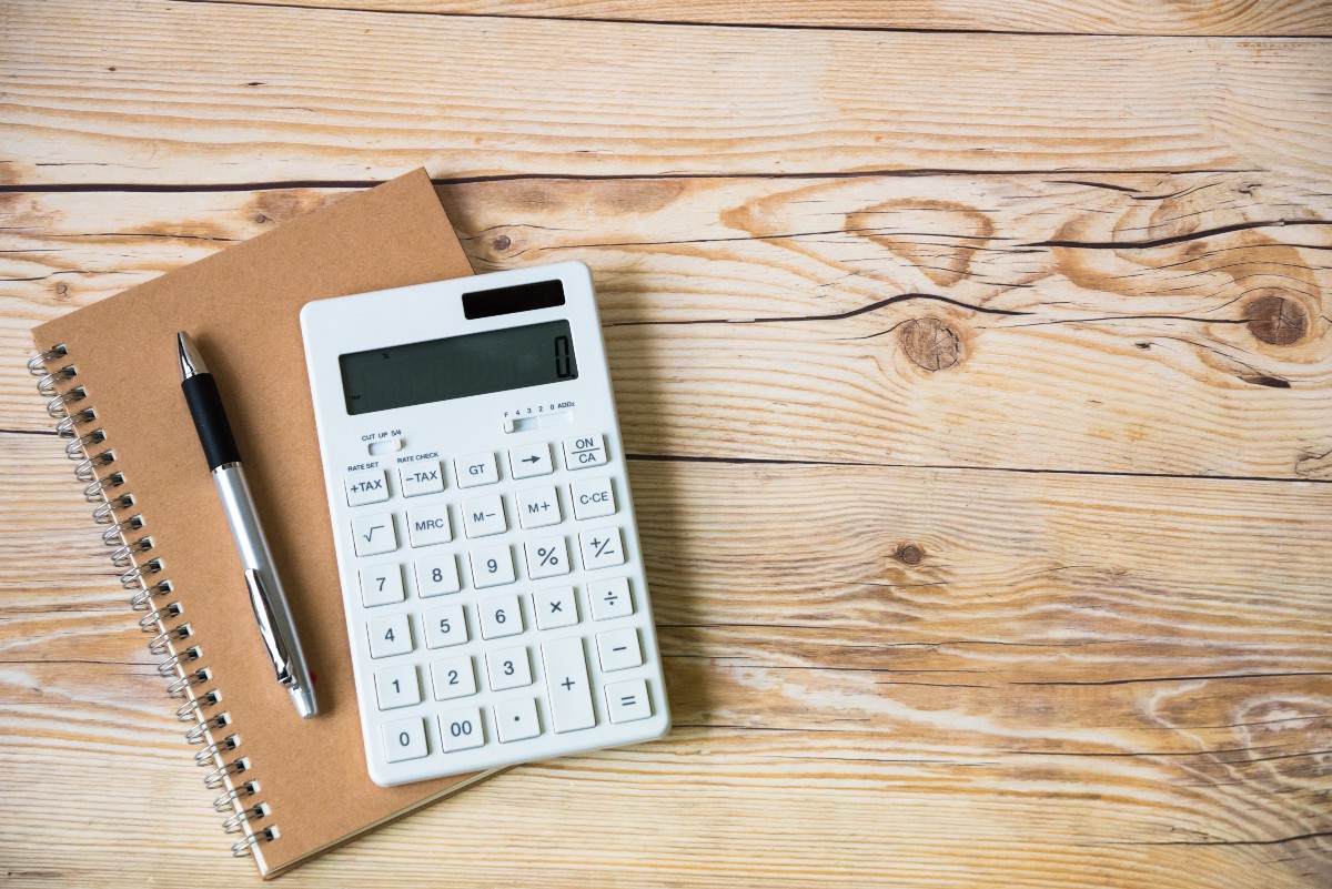 木目のテーブルの上に置かれたノート、ペン、電卓の画像。