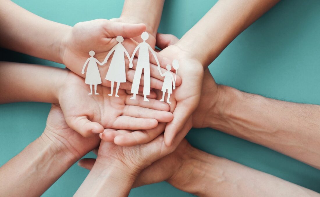 重なり合った手の上に、紙で作られた家族のシルエットが置かれている。