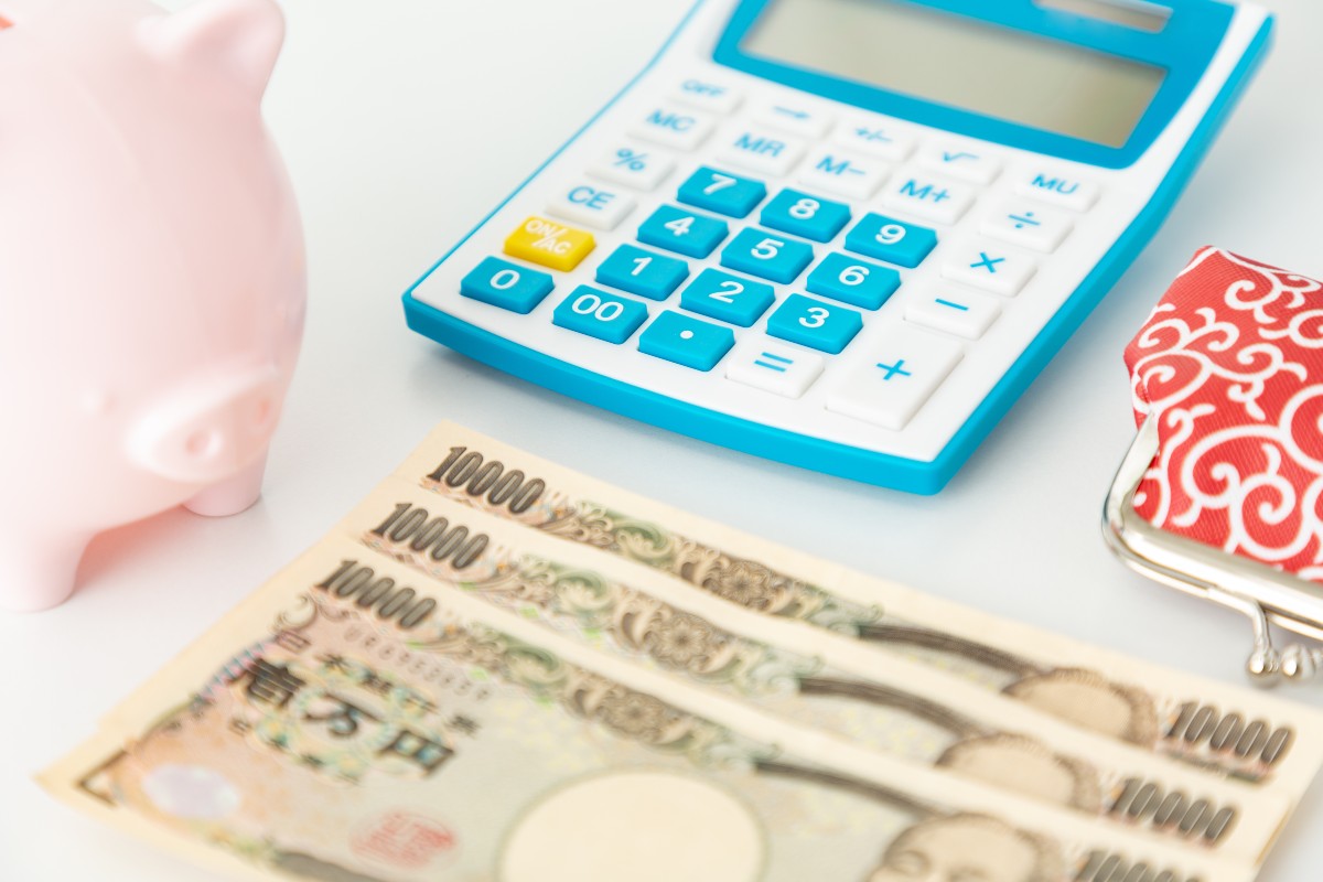 青い電卓と1万円札、ピンクの貯金箱が置かれた机の上のイメージ