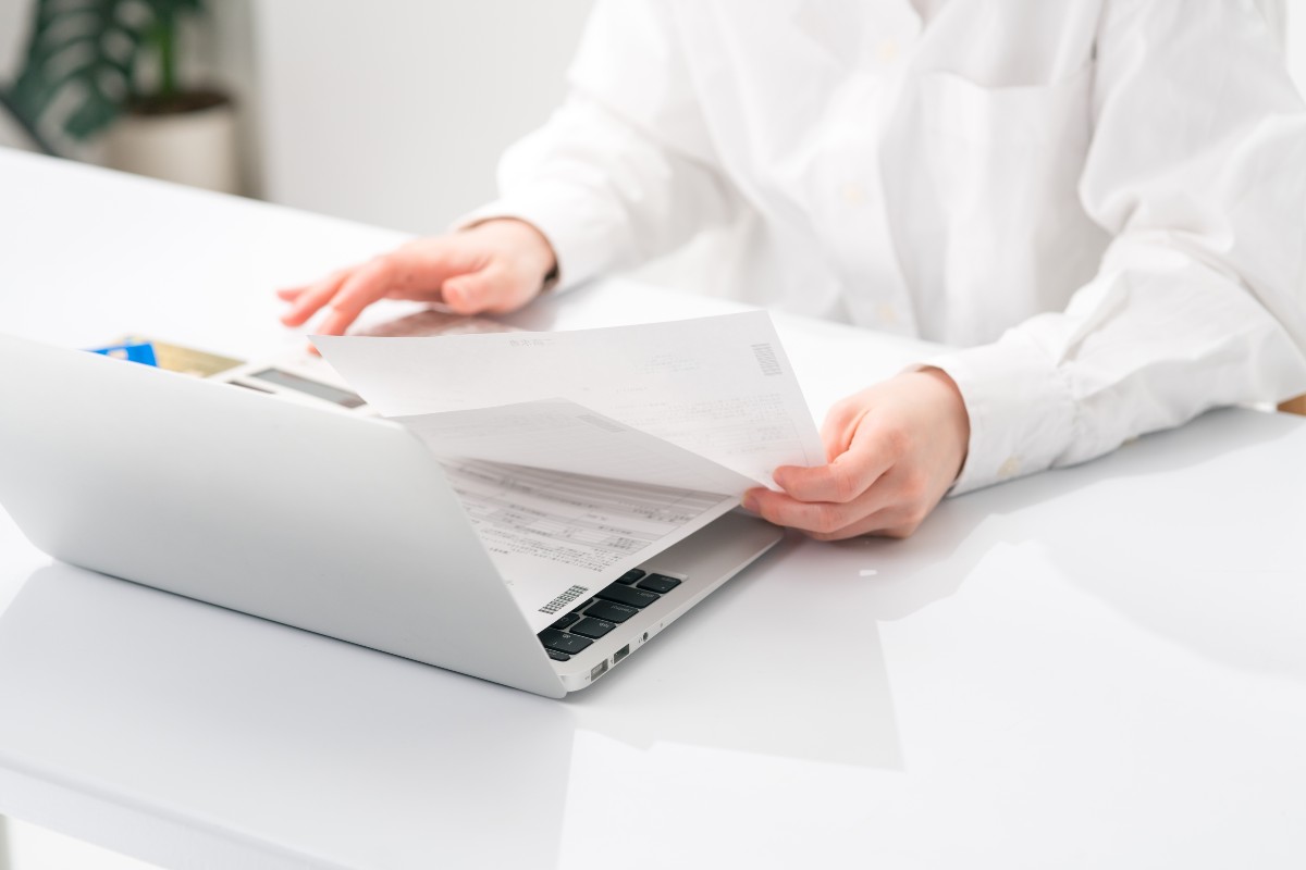 ノートパソコンを前に、書類を確認する人物の手元