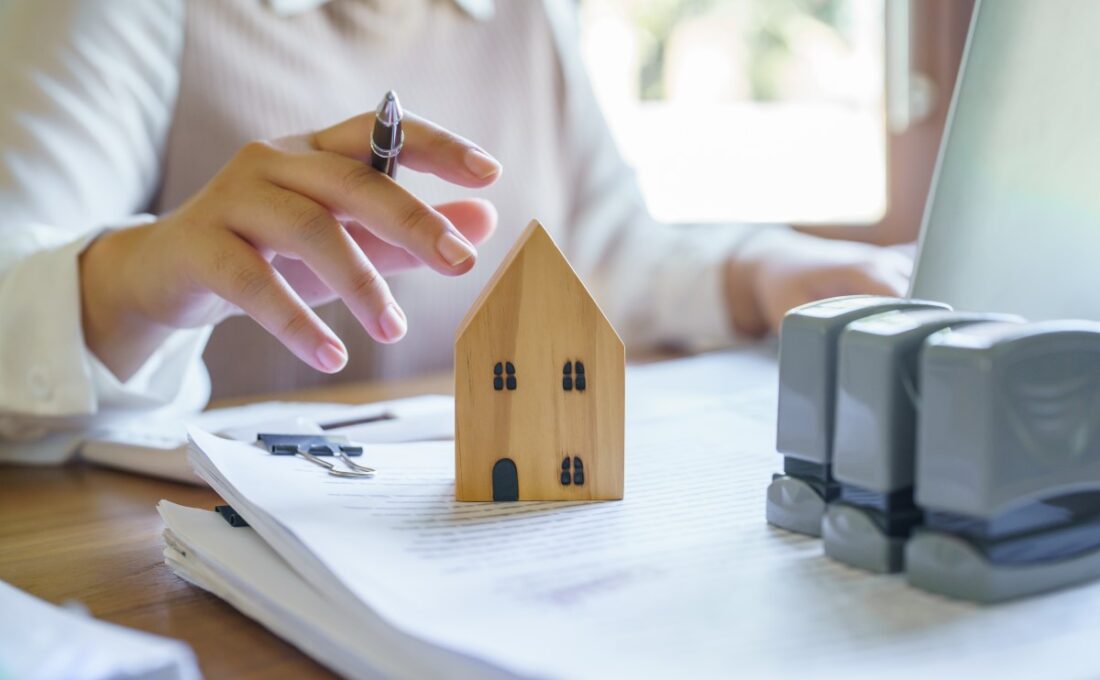 書類と家の模型を扱う人物の手元。契約書の確認や不動産取引を示唆するイメージ。