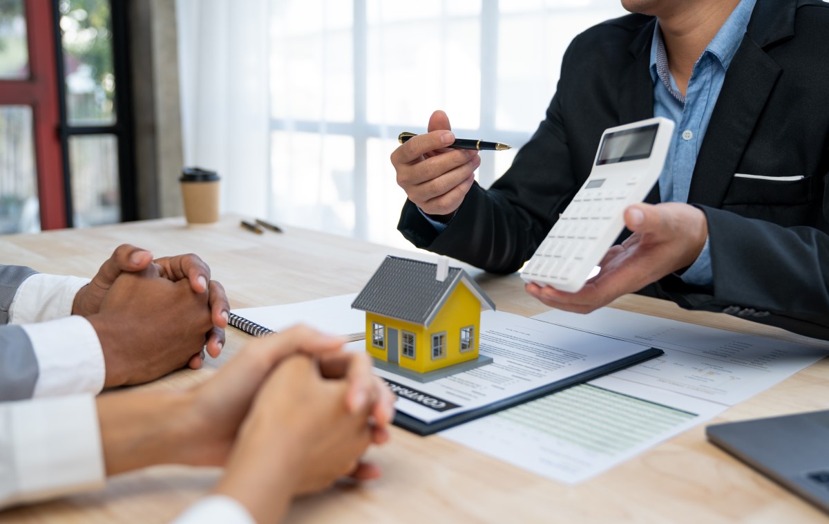 不動産の契約に関する相談をしている場面。ミニチュアの家、電卓、契約書が机に置かれている。