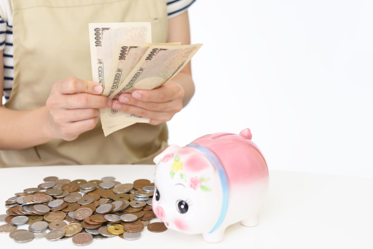 豚の貯金箱の隣で1万円札を数えている手