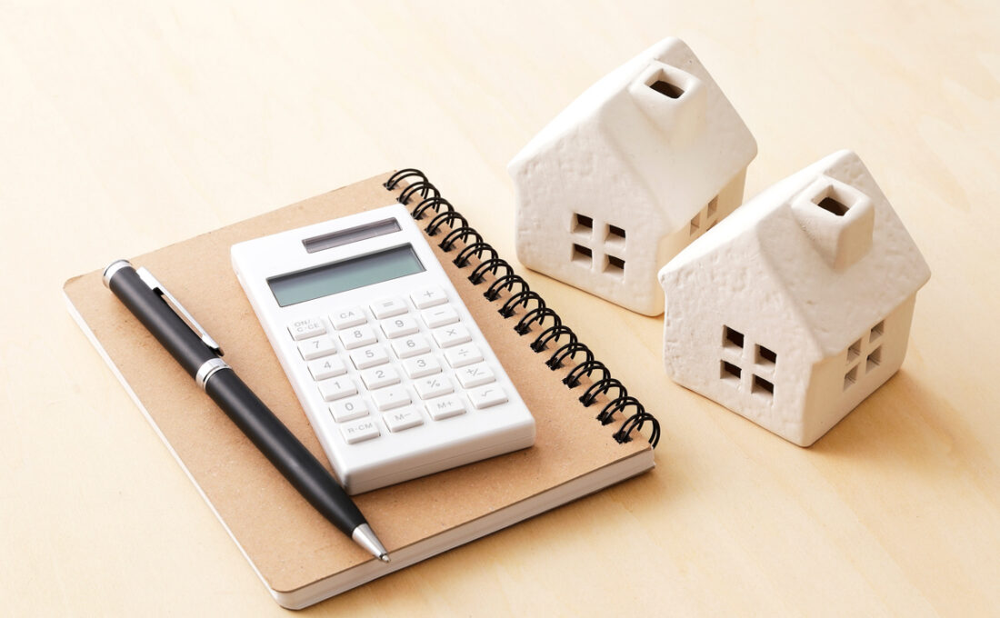 メモ帳、電卓、ペン、そして2つの家の模型が置かれた机の上の風景
