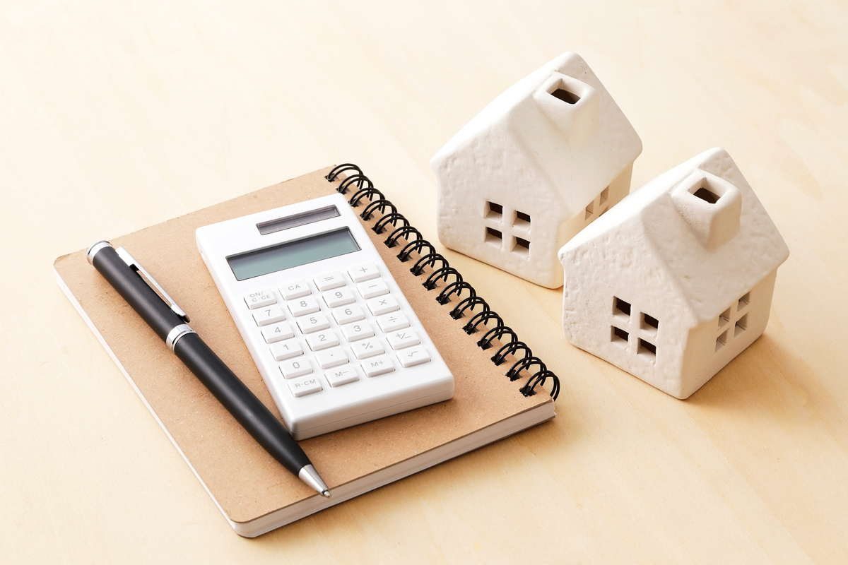 メモ帳、電卓、ペン、そして2つの家の模型が置かれた机の上の風景