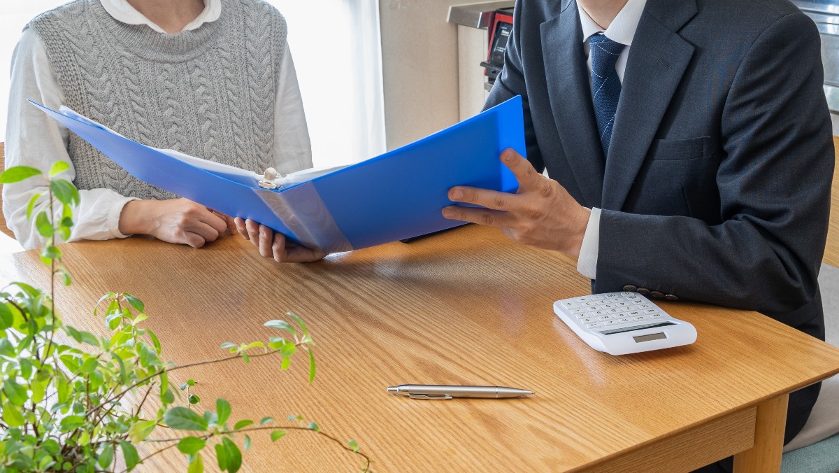 ビジネスマンが青いファイルを開いて、クライアントに説明している場面