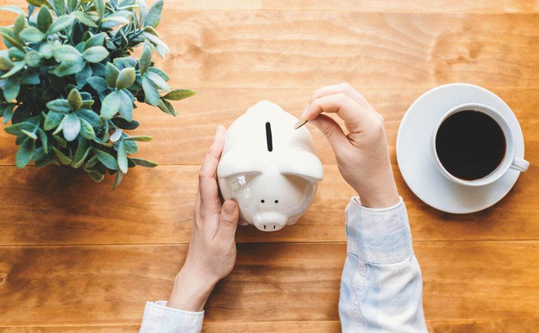 貯金箱にコインを入れる手とコーヒーカップ。
