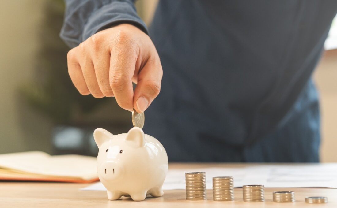 白い貯金箱にコインを入れる手と、並んだコイン