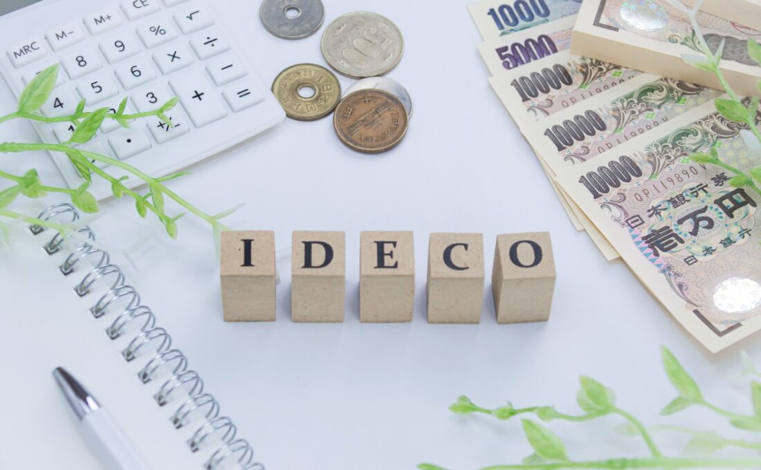 iDeCoと書かれたブロック、電卓、硬貨、紙幣がデスクに並んでいる。