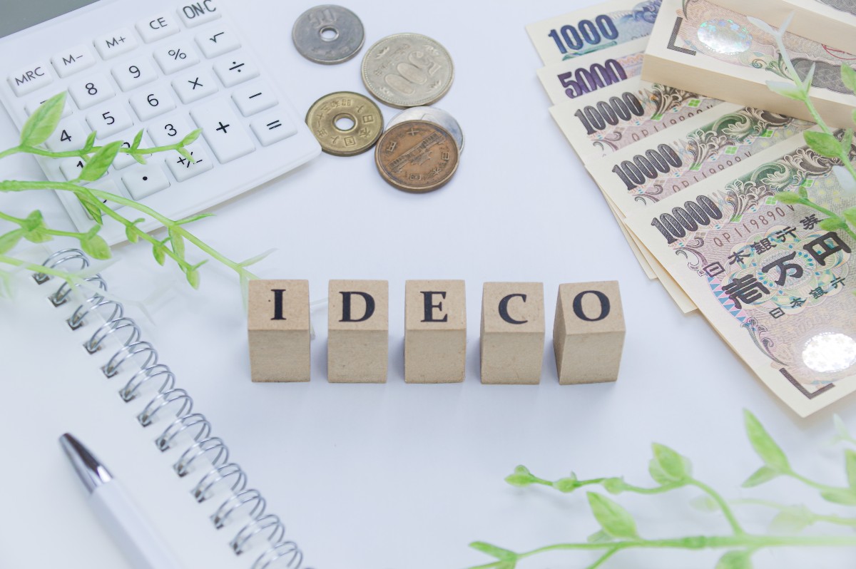 iDeCoと書かれたブロック、電卓、硬貨、紙幣がデスクに並んでいる。