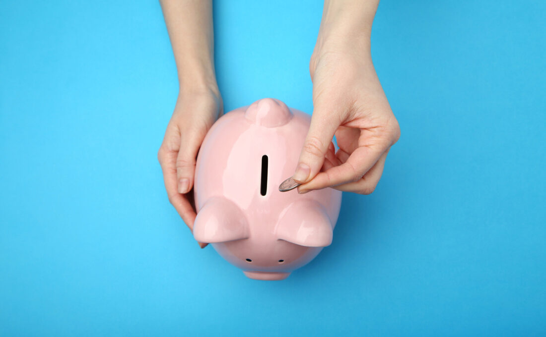 手がピンクの貯金箱にコインを入れている。