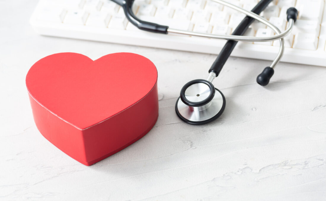 赤いハート型のボックスと聴診器、キーボードが白い背景の上に置かれている医療関連のイメージ