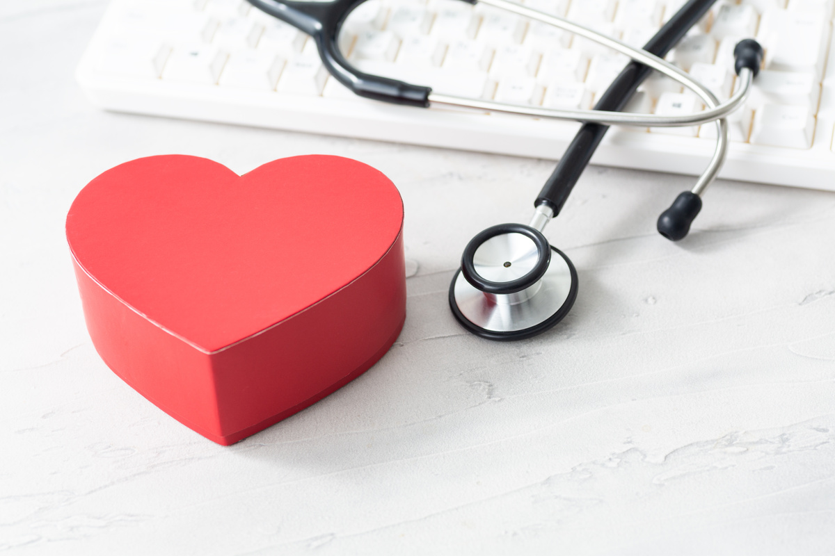 赤いハート型のボックスと聴診器、キーボードが白い背景の上に置かれている医療関連のイメージ