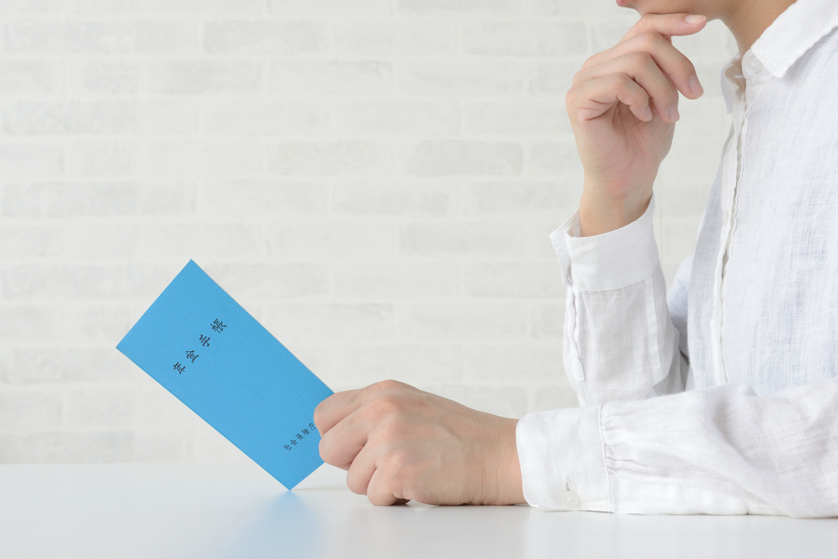 青い年金手帳を持ち、考え込んでいる人物