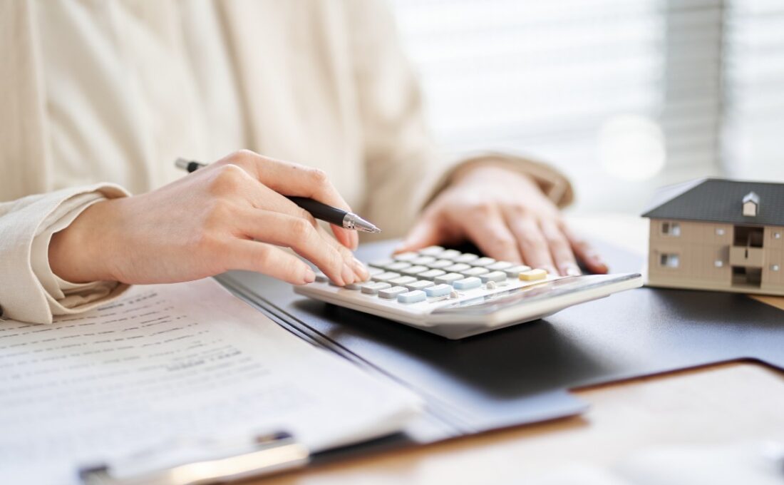電卓で計算をする手と書類、家の模型。