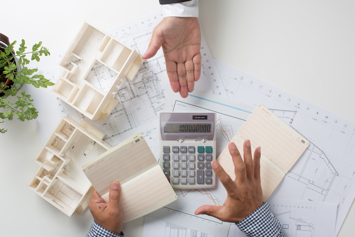 住宅模型、図面、電卓、通帳を使いながら家計について話し合っている人々の手元