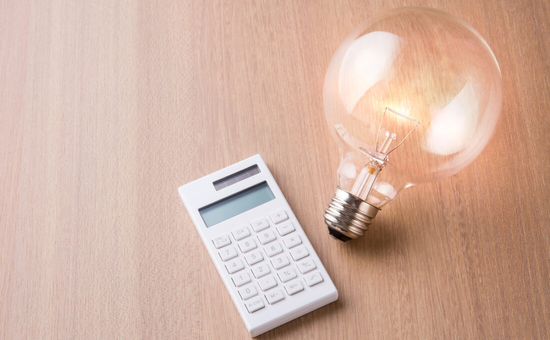 木のテーブルに置かれた電卓と点灯している電球