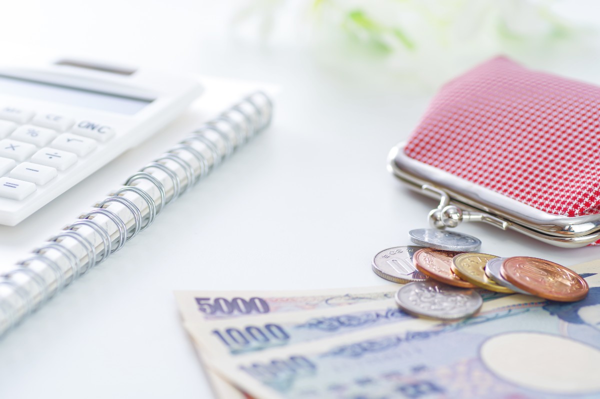 計算機、通帳、コインと紙幣が並んだ机の上