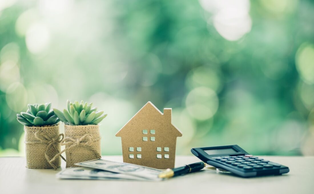 机の上に配置された家の模型、計算機、ドル紙幣、ペン、観葉植物