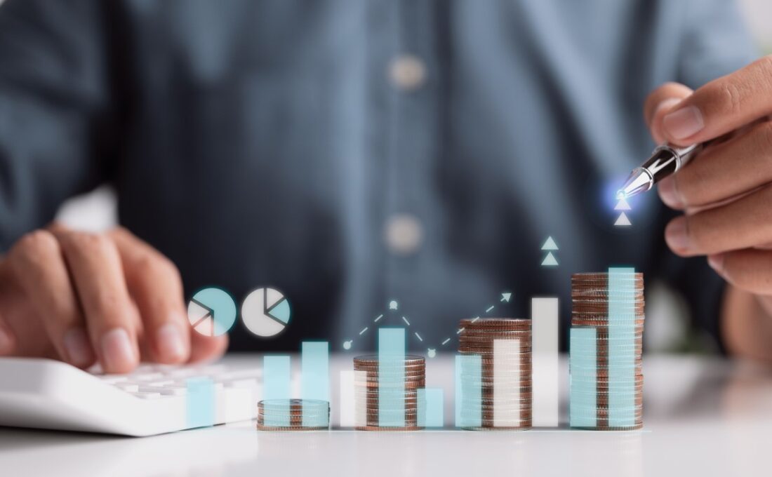 コインの積み重ねと成長を象徴するグラフを指し示すビジネスマン