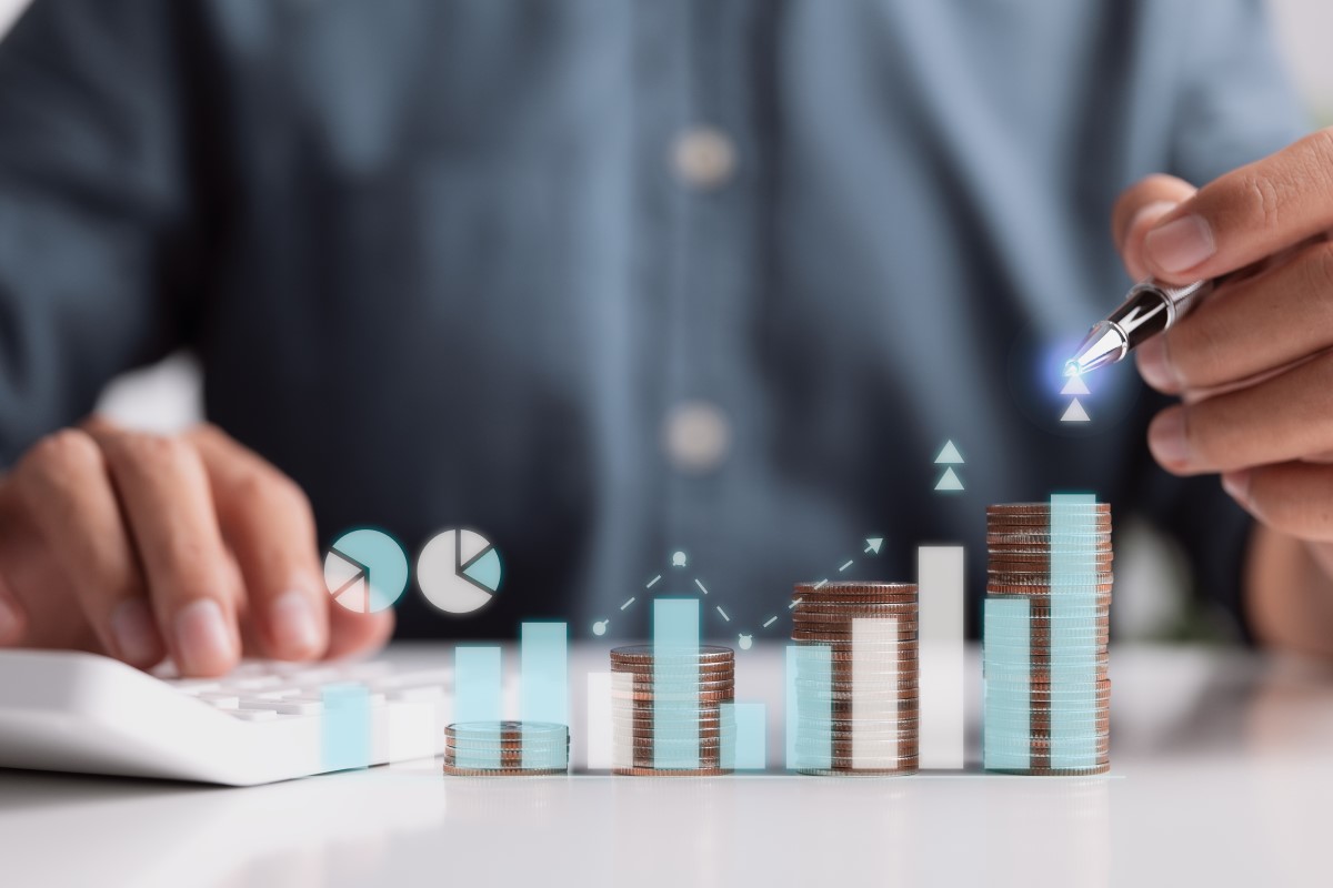 コインの積み重ねと成長を象徴するグラフを指し示すビジネスマン
