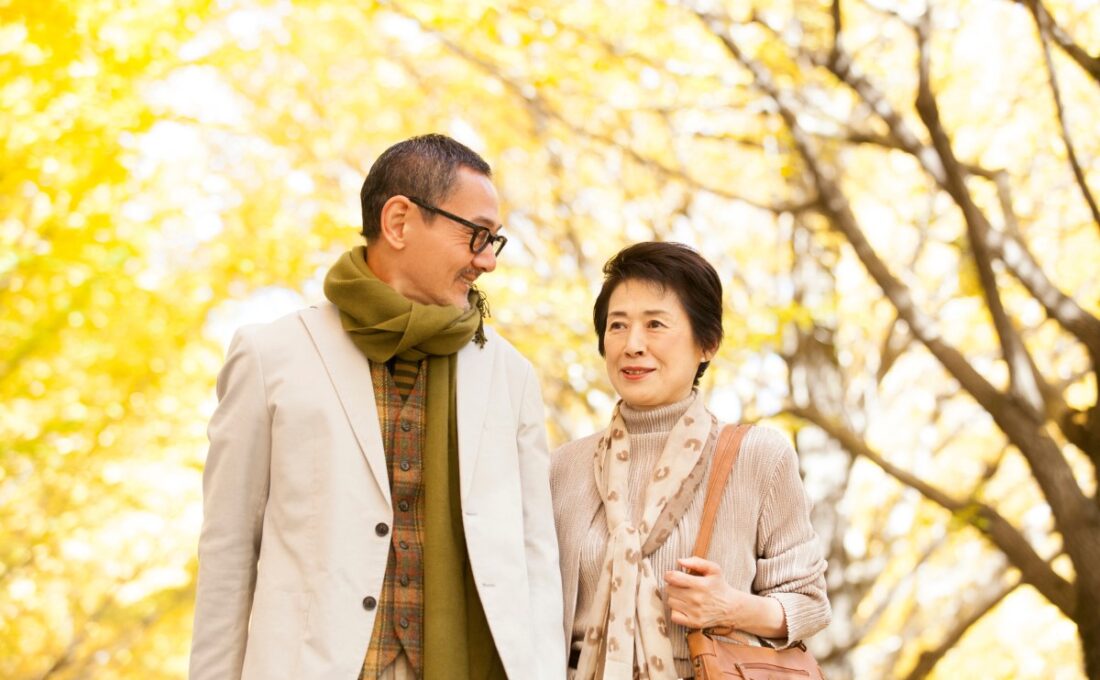 秋の紅葉の中を仲良く歩く高齢夫婦