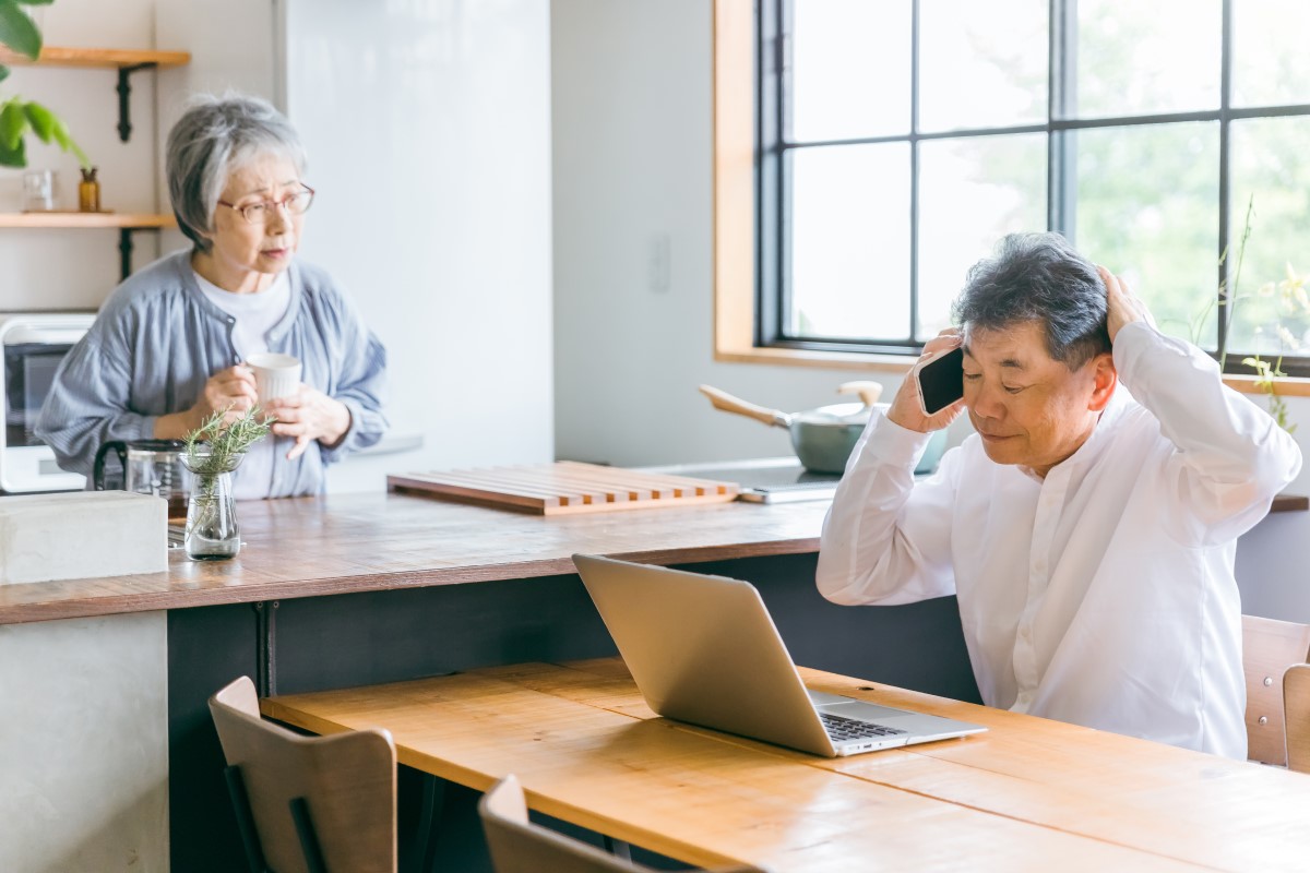 電話しながらパソコンの前で悩む男性とそれを見守る女性