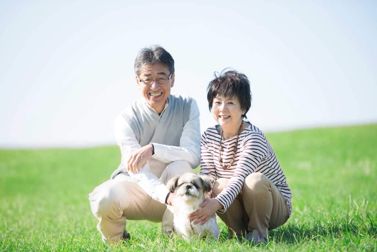 芝生の上で犬を抱きながら微笑む中年の夫婦