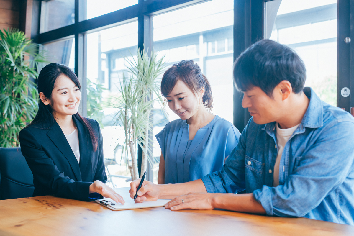 書類にサインするカップルと、その手続きをサポートする担当者。