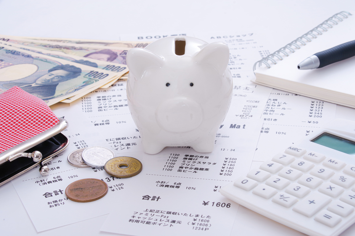貯金箱と日本円の紙幣、硬貨、家計簿。