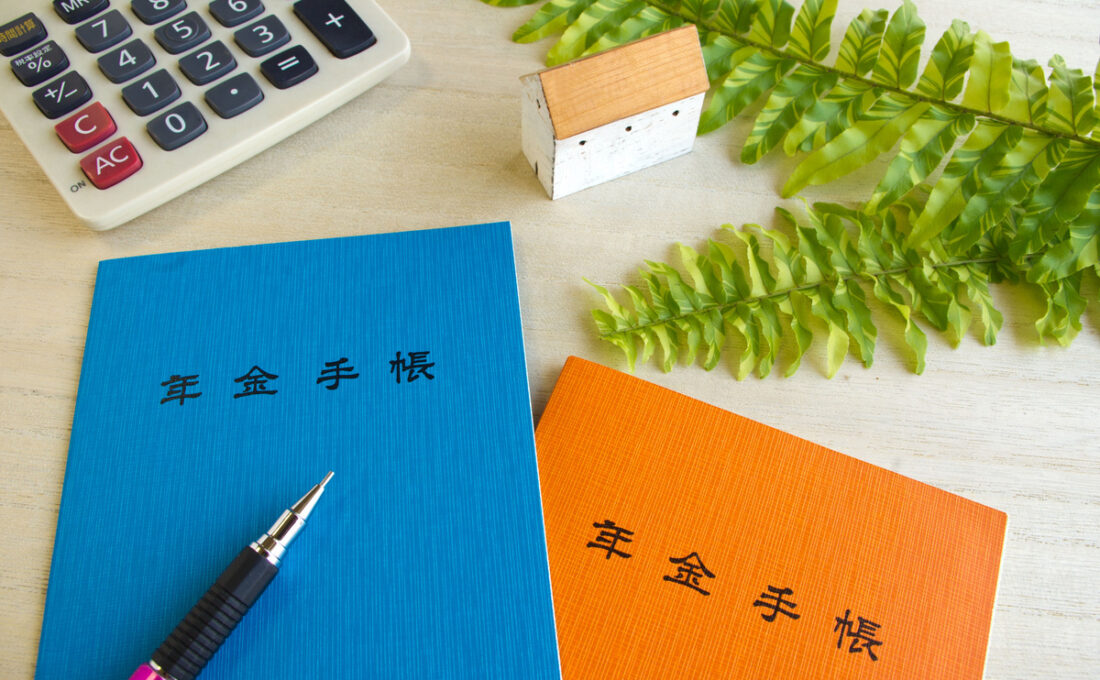 年金手帳、計算機、小さな家の模型が並べられたテーブル