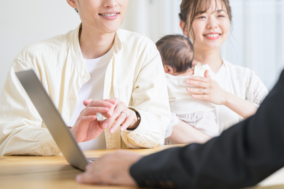 赤ちゃんを抱きながらパソコンの前で相談する若い夫婦
