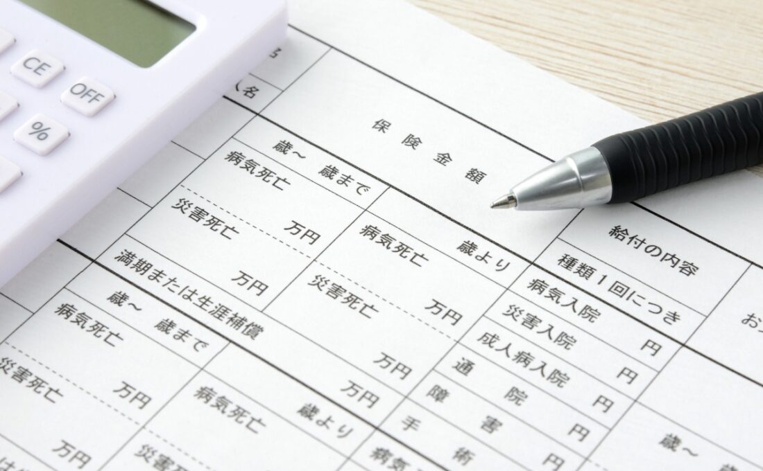 保険の詳細が記載された書類と計算機、ペン