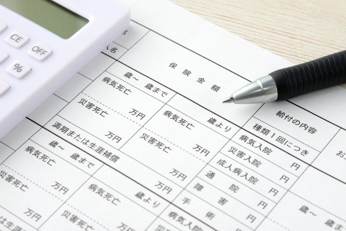 保険の詳細が記載された書類と計算機、ペン