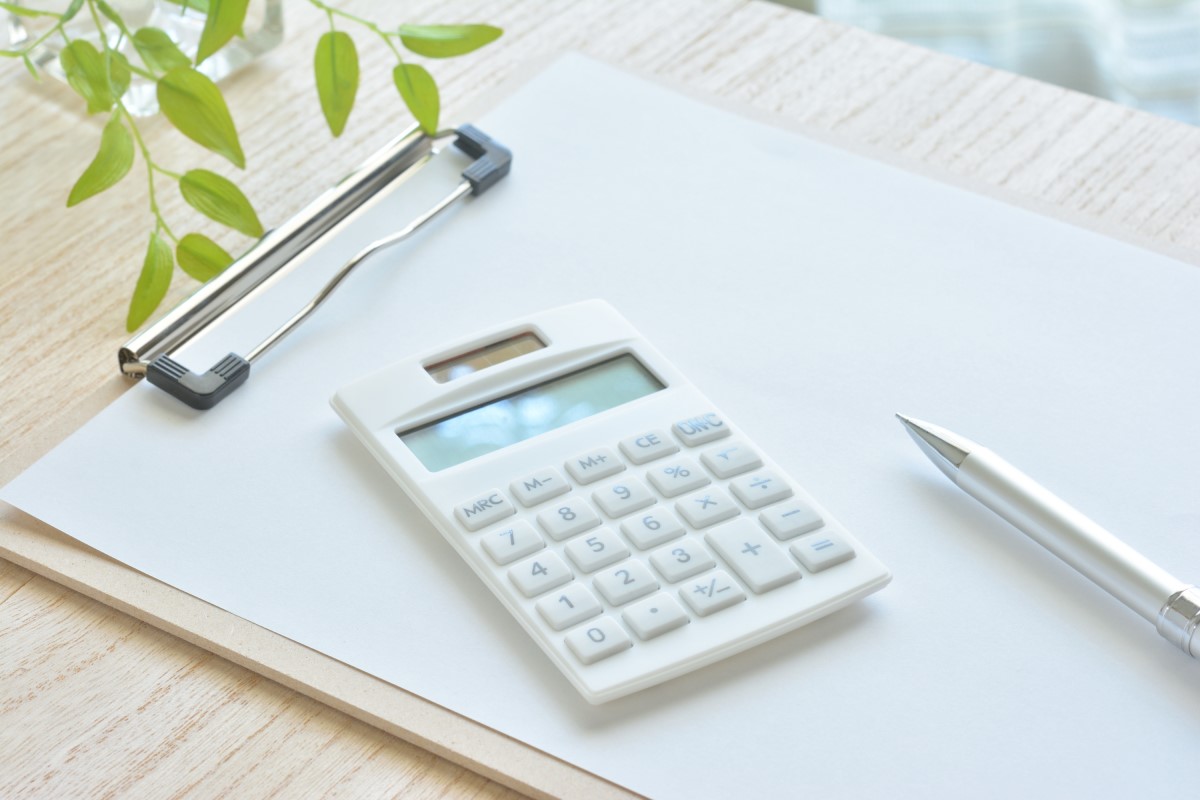 クリップボードと電卓、ペンが置かれた明るいデスク