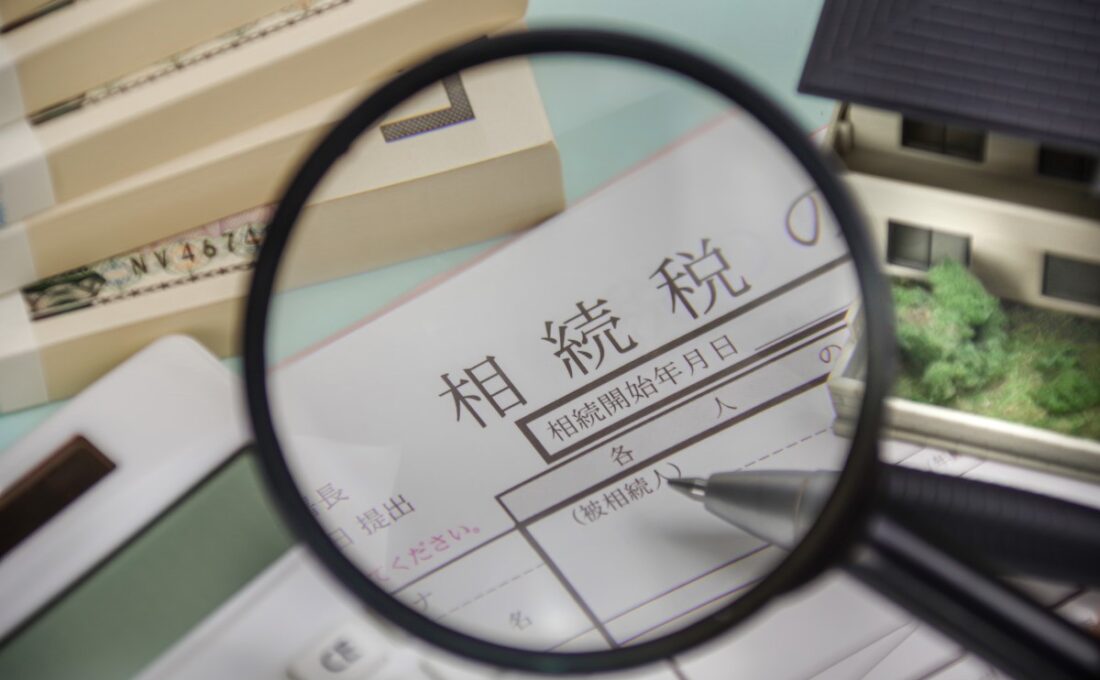 相続税の申告書に拡大鏡をかざし、ペンを持った手元