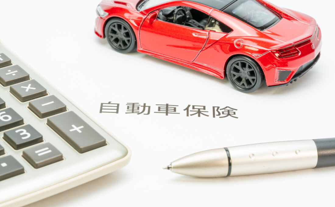 自動車保険の書類と赤い車の模型、計算機とペンが添えられたイメージ