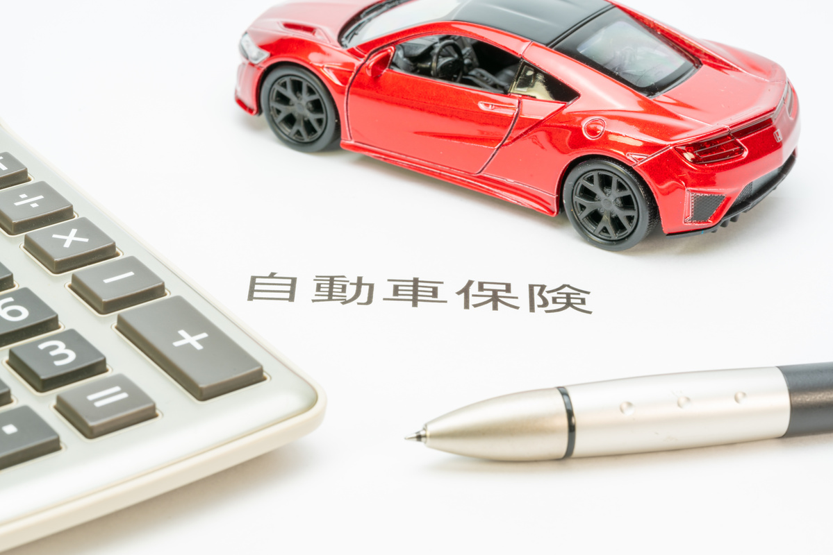 自動車保険の書類と赤い車の模型、計算機とペンが添えられたイメージ