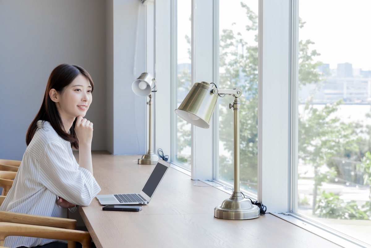 窓際で外を見ながらパソコンを触っている女性